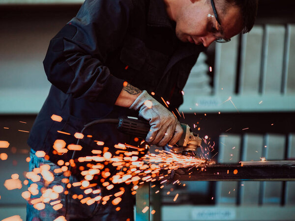 Heavy Industry Engineering Factory Interior with Industrial Worker Using Angle Grinder and Cutting a Metal Tube. Contractor in Safety Uniform and Hard Hat Manufacturing Metal Structures. High-quality