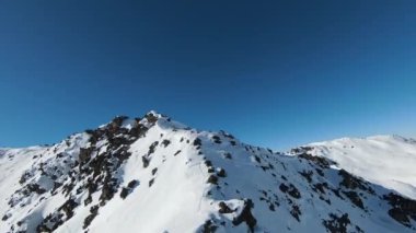 Havadan izleme sporu FPV İHA 'sı dağın tepesine yükseliyor. Alplerin güzel zirveleri kar örtüsüyle kaplıdır. Yüksek kalite 4k görüntü