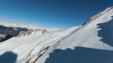 Havadan izleme sporu FPV İHA 'sı dağın tepesine yükseliyor. Alplerin güzel zirveleri kar örtüsüyle kaplıdır. Yüksek kalite 4k görüntü