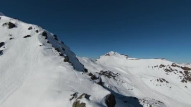 Havadan izleme sporu FPV İHA 'sı dağın tepesine yükseliyor. Alplerin güzel zirveleri kar örtüsüyle kaplıdır. Yüksek kalite 4k görüntü