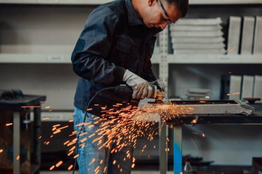 Heavy Industry Engineering Factory Interior with Industrial Worker Using Angle Grinder and Cutting a Metal Tube. Güvenlik Üniforması ve Sert Şapka Üretim Metal Yapıları Müteahhiti. Yüksek kalite