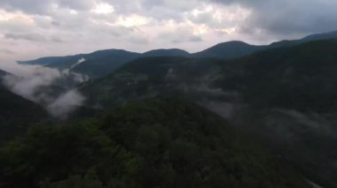 Yağmur mevsiminde yağmur bulutlarıyla dolu yemyeşil tropikal orman dağının üzerinde uçan hava manzaralı Doi Phuka Dağı kuzey Tayland 'daki rezerve edilmiş ulusal park. Yüksek kalite 4k