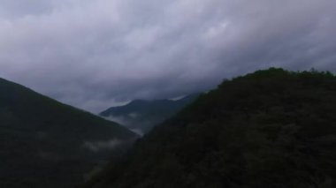 Yağmur mevsiminde yağmur bulutlarıyla dolu yemyeşil tropikal orman dağının üzerinde uçan hava manzaralı Doi Phuka Dağı kuzey Tayland 'daki rezerve edilmiş ulusal park. Yüksek kalite 4k