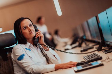 Female security guard operator talking on the phone while working at the workstation with multiple displays Security guards working on multiple monitors. High quality photo