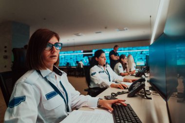 Veri kontrol odasında çalışan bir grup kadın güvenlik operatörü. Çalışma istasyonunda birden fazla ekranla çalışan teknik operatörler. Güvenlik görevlileri birden fazla monitörde çalışıyor.