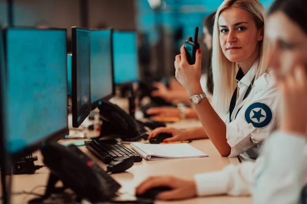 Female security operator holding portable radio in hand while working in a data system control room offices Technical Operator Working at the workstation with multiple displays, a security guard