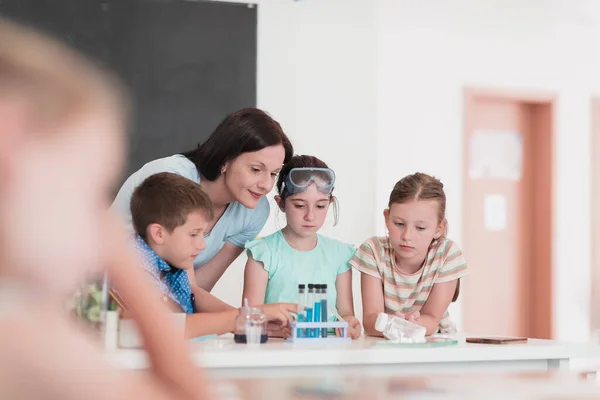 Elementary School Science Classroom: Enthusiastic Teacher Explains Chemistry to Diverse Group of Children, Little girl Mixes Chemicals in Beakers. Children Learn with Interest. Hi quality stock photo.