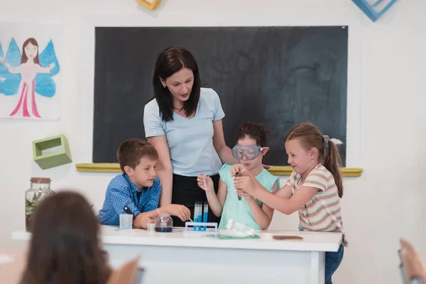 Elementary School Science Classroom: Enthusiastic Teacher Explains Chemistry to Diverse Group of Children, Little girl Mixes Chemicals in Beakers. Children Learn with Interest. Hi quality stock photo.
