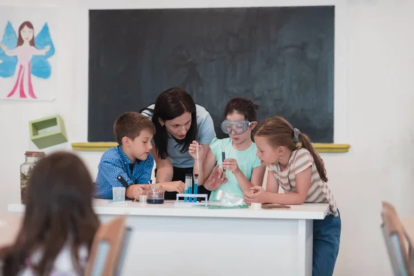 Elementary School Science Classroom: Enthusiastic Teacher Explains Chemistry to Diverse Group of Children, Little girl Mixes Chemicals in Beakers. Children Learn with Interest. Hi quality stock photo.