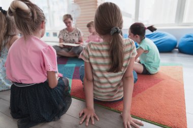 Reading time in elementary school or kindergarten, teacher reading a book to kids in elementary school or kindergarten. Selective focus. High quality photo