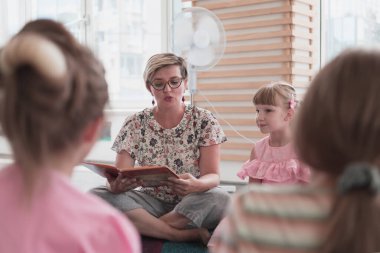 Reading time in elementary school or kindergarten, teacher reading a book to kids in elementary school or kindergarten. Selective focus. High quality photo