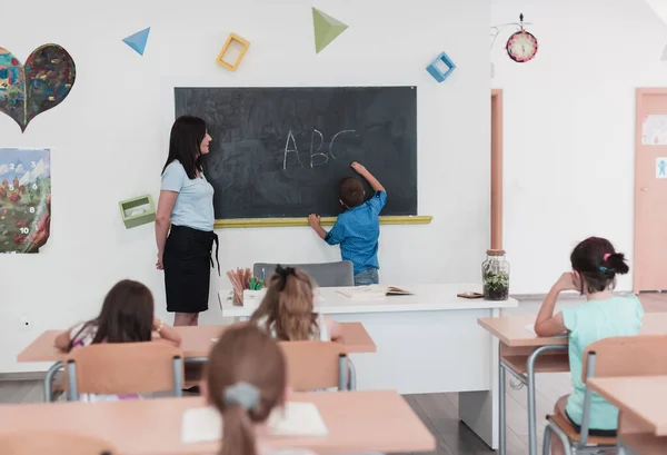 Elementary School Female Teacher Helps Child Student While Writing Answer — стоковое фото