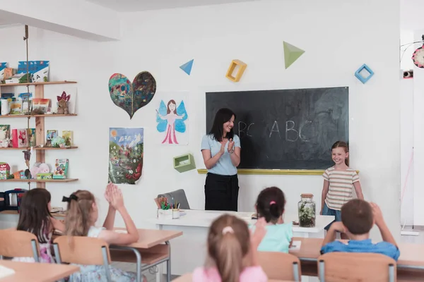 Elementary School Female Teacher Helps Child Student While Writing Answer — Foto Stock