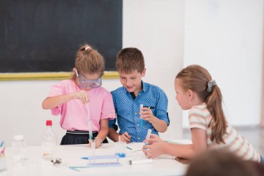 Elementary School Science Classroom: Enthusiastic Teacher Explains Chemistry to Diverse Group of Children, Little Boy Mixes Chemicals in Beakers. Children Learn with Interest. High quality photo