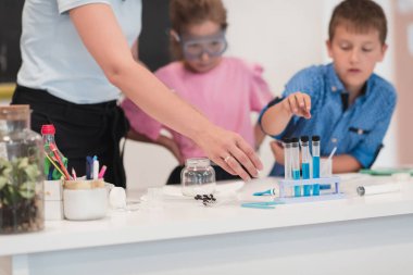 Elementary School Science Classroom: Enthusiastic Teacher Explains Chemistry to Diverse Group of Children, Little Boy Mixes Chemicals in Beakers. Children Learn with Interest. High quality photo