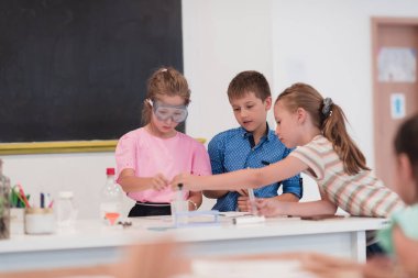 Elementary School Science Classroom: Enthusiastic Teacher Explains Chemistry to Diverse Group of Children, Little Boy Mixes Chemicals in Beakers. Children Learn with Interest. High quality photo