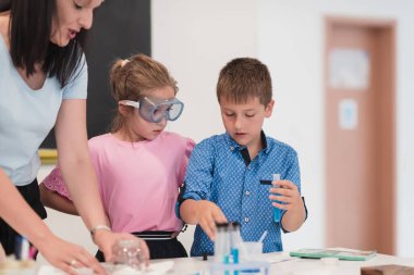 Elementary School Science Classroom: Enthusiastic Teacher Explains Chemistry to Diverse Group of Children, Little Boy Mixes Chemicals in Beakers. Children Learn with Interest. High quality photo