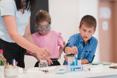 Elementary School Science Classroom: Enthusiastic Teacher Explains Chemistry to Diverse Group of Children, Little Boy Mixes Chemicals in Beakers. Children Learn with Interest. High quality photo