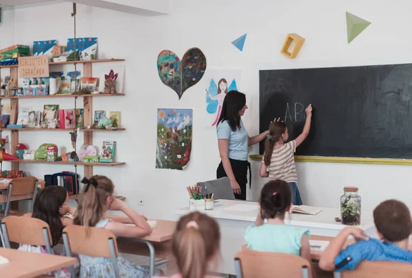 Elementary School Female Teacher Helps Child Student While Writing Answer — Stockfoto