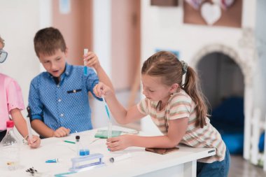 Elementary School Science Classroom: Enthusiastic Teacher Explains Chemistry to Diverse Group of Children, Little Boy Mixes Chemicals in Beakers. Children Learn with Interest. High quality photo