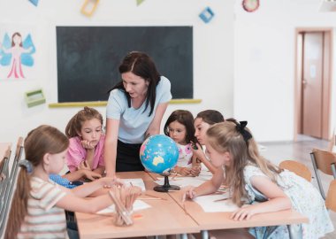Female teacher with kids in geography class looking at a globe. Side view of a group of diverse happy school kids with a globe in the classroom at school. High quality photo