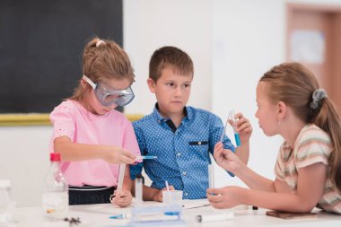 Elementary School Science Classroom: Enthusiastic Teacher Explains Chemistry to Diverse Group of Children, Little Boy Mixes Chemicals in Beakers. Children Learn with Interest. High quality photo