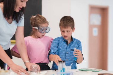 Elementary School Science Classroom: Enthusiastic Teacher Explains Chemistry to Diverse Group of Children, Little Boy Mixes Chemicals in Beakers. Children Learn with Interest. High quality photo