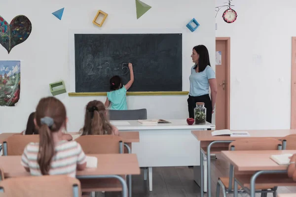 Elementary School Female Teacher Helps Child Student While Writing Answer — Fotografia de Stock