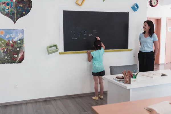 Elementary School Female Teacher Helps Child Student While Writing Answer — Fotografia de Stock