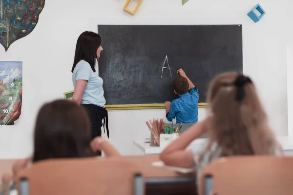 Початкова Школа Жінка Вчителька Допомагає Дитині Під Час Написання Відповіді — стокове фото