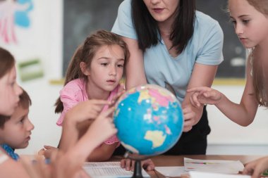 Coğrafya sınıfında coğrafya dersi alan bir bayan öğretmen küreye bakıyor. Okuldaki sınıflarında küresi olan bir grup mutlu okul öğrencisinin yan görüntüsü. Yüksek kalite fotoğraf