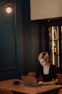 Businesswoman sitting in a cafe while focused on working on a laptop and participating in online meetings. Selective focus. High quality photo. 