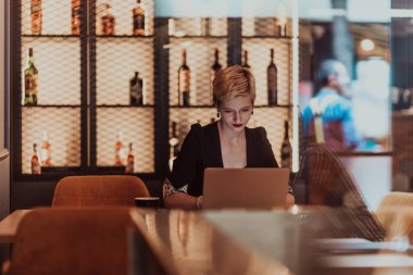 Businesswoman sitting in a cafe while focused on working on a laptop and participating in online meetings. Selective focus. High quality photo. 