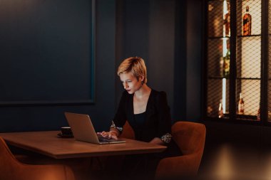 Businesswoman sitting in a cafe while focused on working on a laptop and participating in online meetings. Selective focus. High quality photo. 