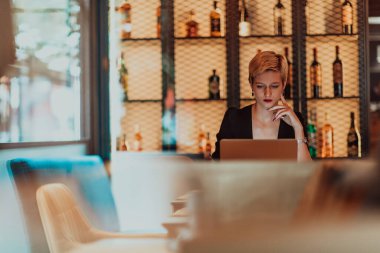 Businesswoman sitting in a cafe while focused on working on a laptop and participating in online meetings. Selective focus. High quality photo. 