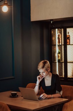 Businesswoman sitting in a cafe while focused on working on a laptop and participating in online meetings. Selective focus. High quality photo. 