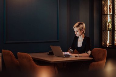 Businesswoman sitting in a cafe while focused on working on a laptop and participating in online meetings. Selective focus. High quality photo. 