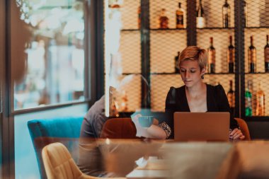 Businesswoman sitting in a cafe while focused on working on a laptop and participating in online meetings. Selective focus. High quality photo. 