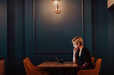 Businesswoman sitting in a cafe while focused on working on a laptop and participating in online meetings. Selective focus. High quality photo. 