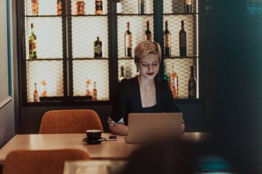 Businesswoman sitting in a cafe while focused on working on a laptop and participating in online meetings. Selective focus. High quality photo. 