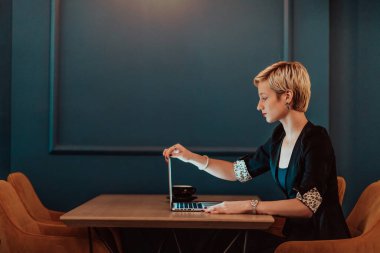 Businesswoman sitting in a cafe while focused on working on a laptop and participating in online meetings. Selective focus. High quality photo. 