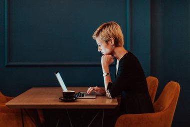 Businesswoman sitting in a cafe while focused on working on a laptop and participating in online meetings. Selective focus. High quality photo. 