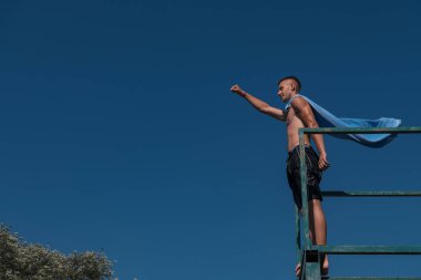 young teen boy near the river having fun with friends at a summer party wearing towel as a superhero scarf ready for a jump looking brave in distance. High quality photo