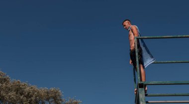 young teen boy near the river having fun with friends at a summer party wearing towel as a superhero scarf ready for a jump looking brave in distance. High quality photo