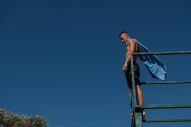 young teen boy near the river having fun with friends at a summer party wearing towel as a superhero scarf ready for a jump looking brave in distance. High quality photo