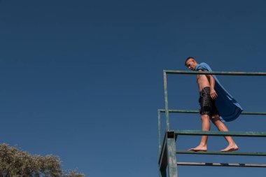 young teen boy near the river having fun with friends at a summer party wearing towel as a superhero scarf ready for a jump looking brave in distance. High quality photo