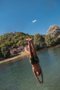 Young teen boy jumping flying and diving in the river. Clear blue sky and trees in distance as a natural background. High quality photo