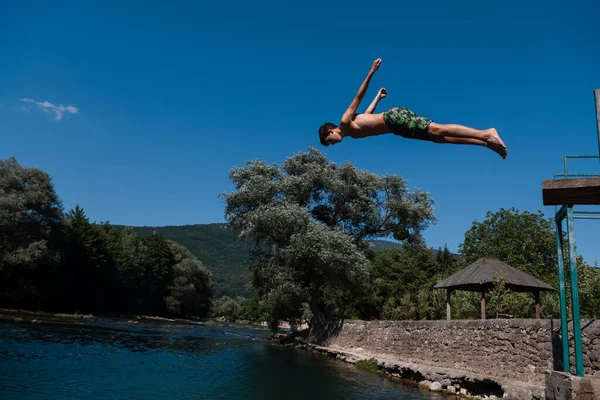 Young teen boy jumping flying and diving in the river. Clear blue sky and trees in distance as a natural background. High quality photo