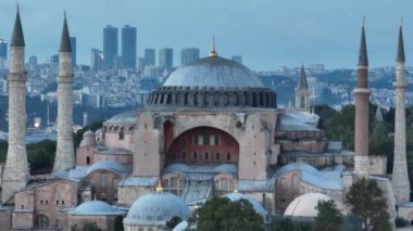 Establishing orbiting aerial drone shot of a Hagia Sophia Holy Grand Mosque with Bosphorus bridge and city skyline with a flag on the background in Fatih, Istanbul, Turkey at sunset. Cinematic footage