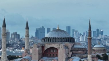 Establishing orbiting aerial drone shot of a Hagia Sophia Holy Grand Mosque with Bosphorus bridge and city skyline with a flag on the background in Fatih, Istanbul, Turkey at sunset. Cinematic footage